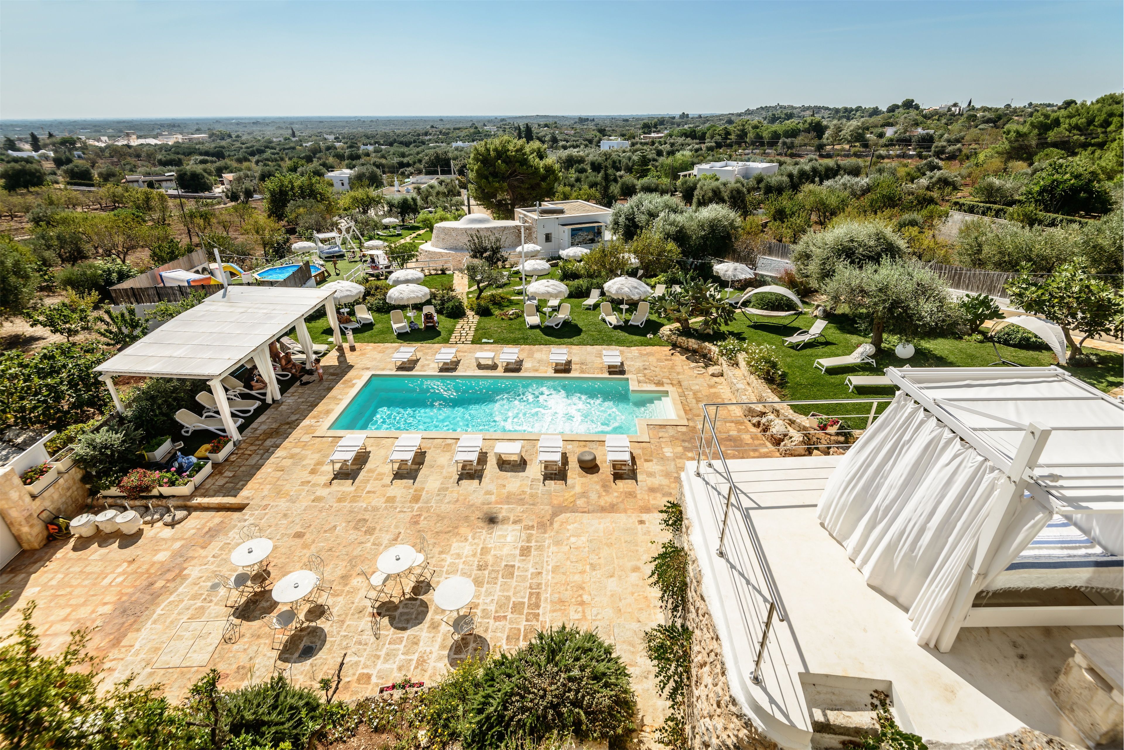 A pool area with lounge chairs and umbrellas, surrounded by greenery and a view of the countryside.