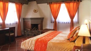 Un dormitorio con cama, escritorio, chimenea y cortinas naranjas.