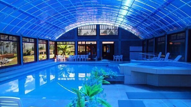 Una piscina interior con techo de cristal, sillones de descanso y una zona de estar.