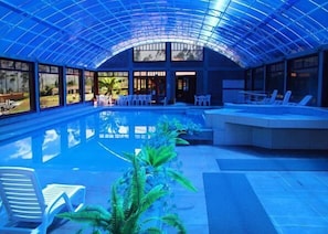 Una piscina interior con techo de cristal, sillones de descanso y una zona de estar.
