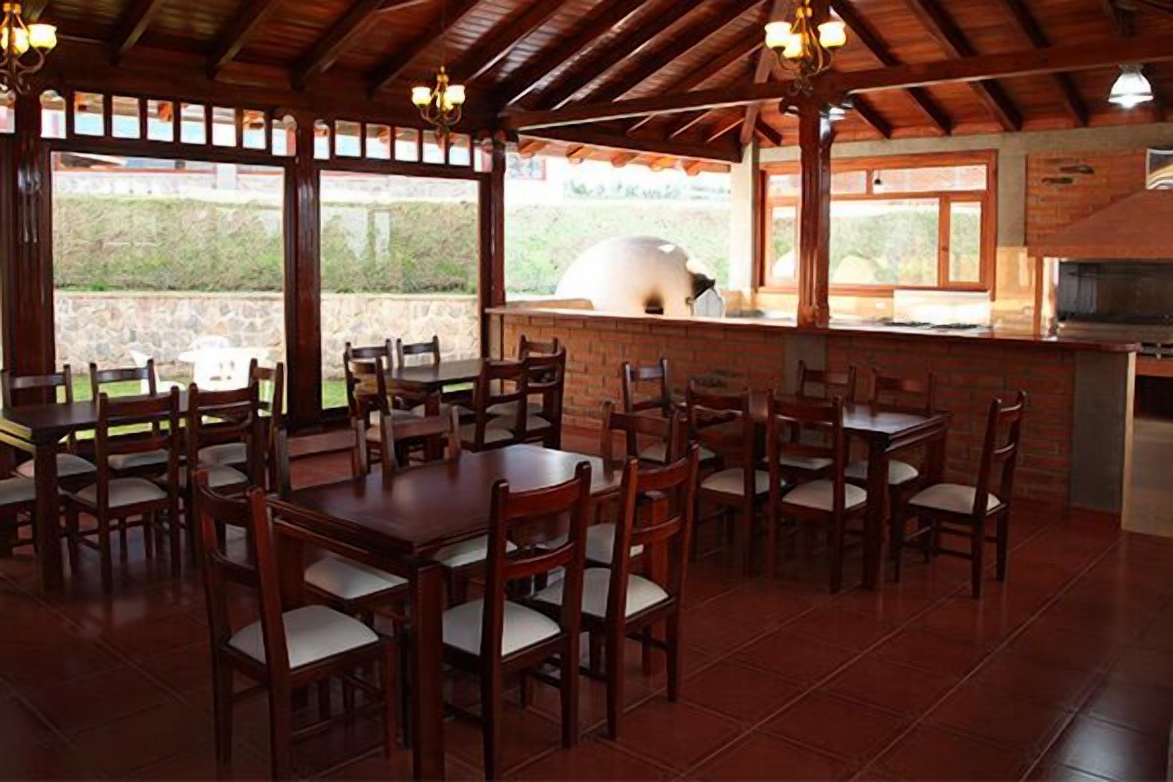 A restaurant with wooden tables and chairs, a brick wall, and a large oven.