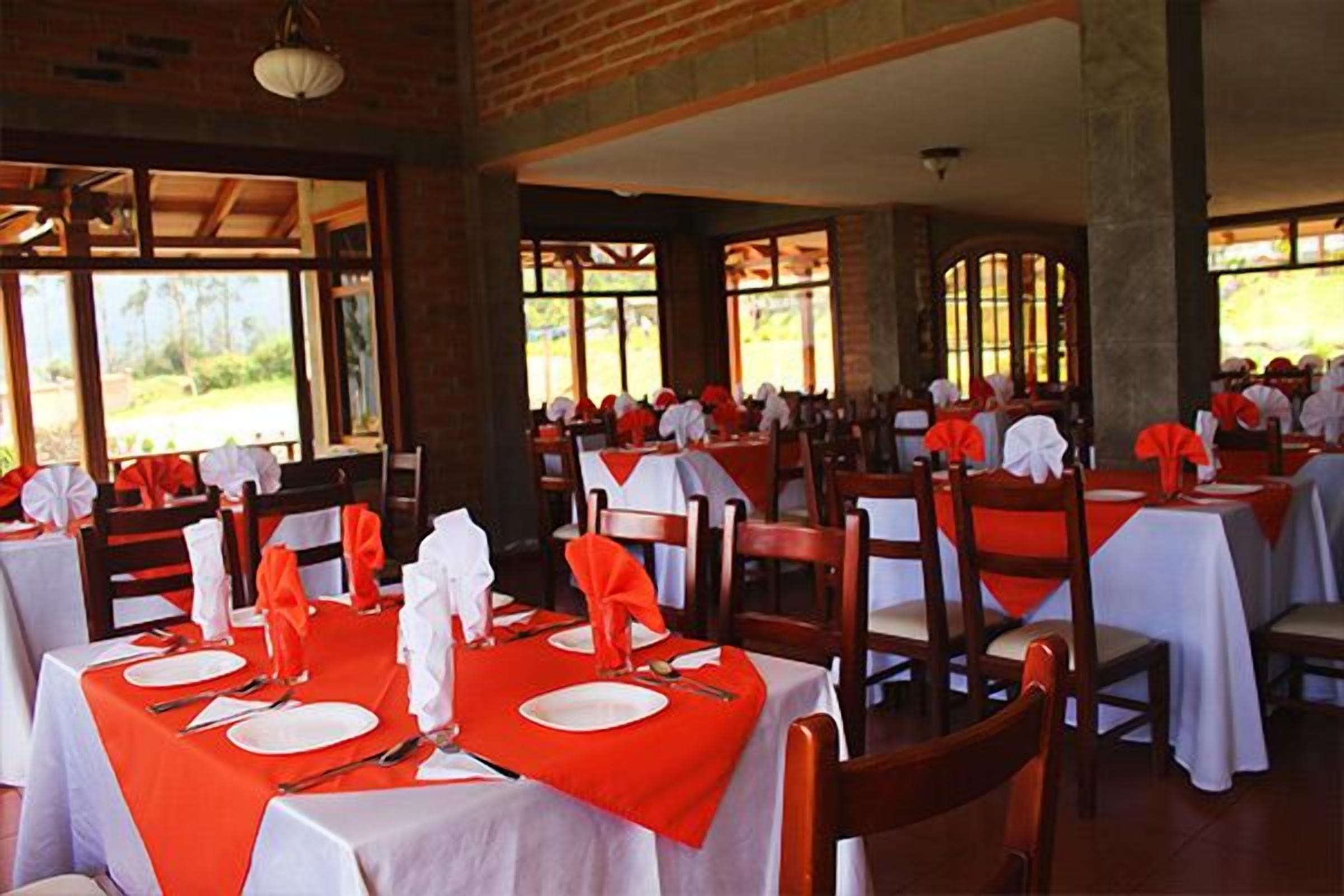Comedor con mesas dispuestas para varios comensales, con manteles rojos y servilletas blancas.