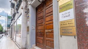 A building facade with a large wooden door, multiple signs, and a sidewalk. - B&B Cairoli (Messina)