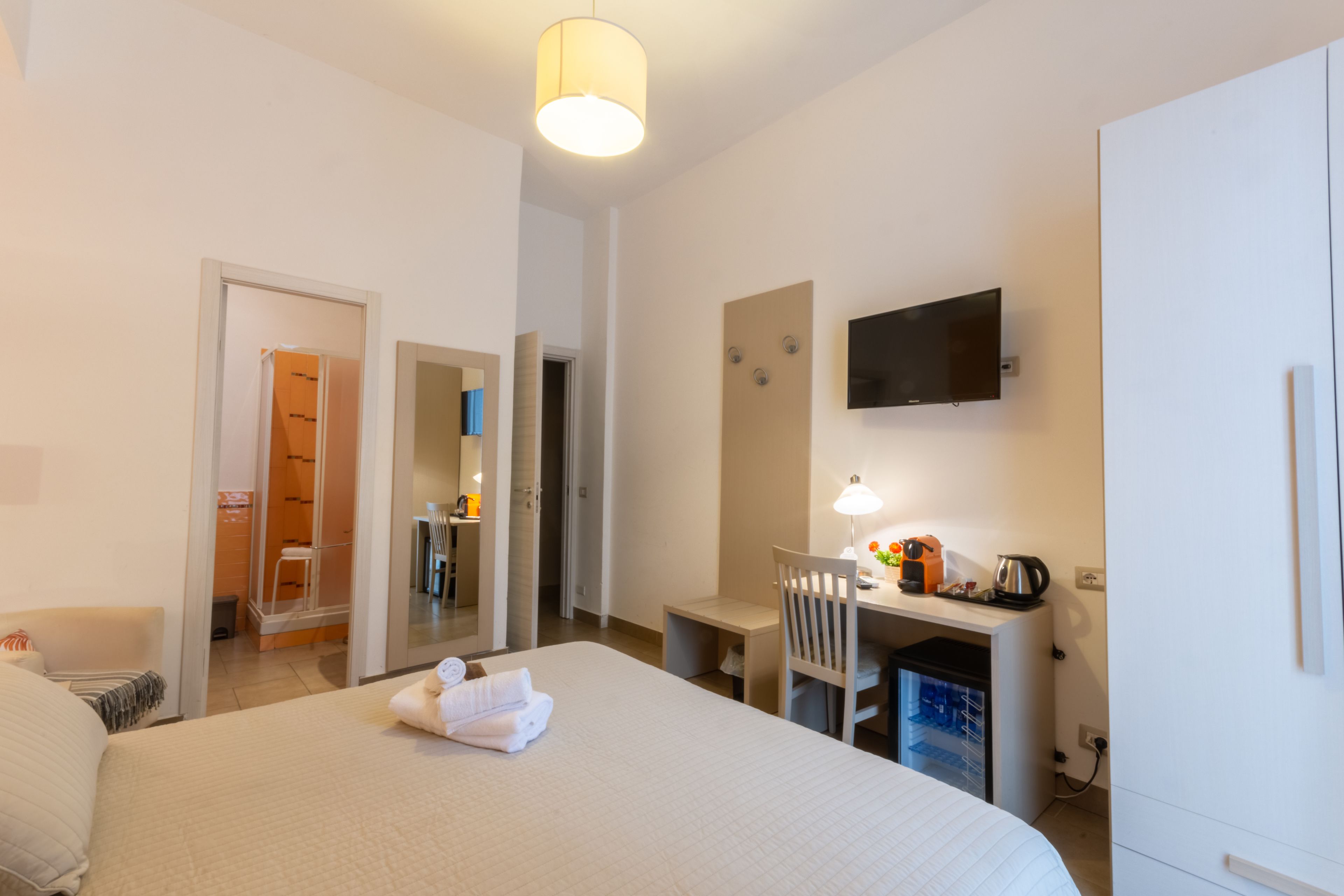 Habitación de hotel con cama, escritorio, silla, televisor y kitchenette.