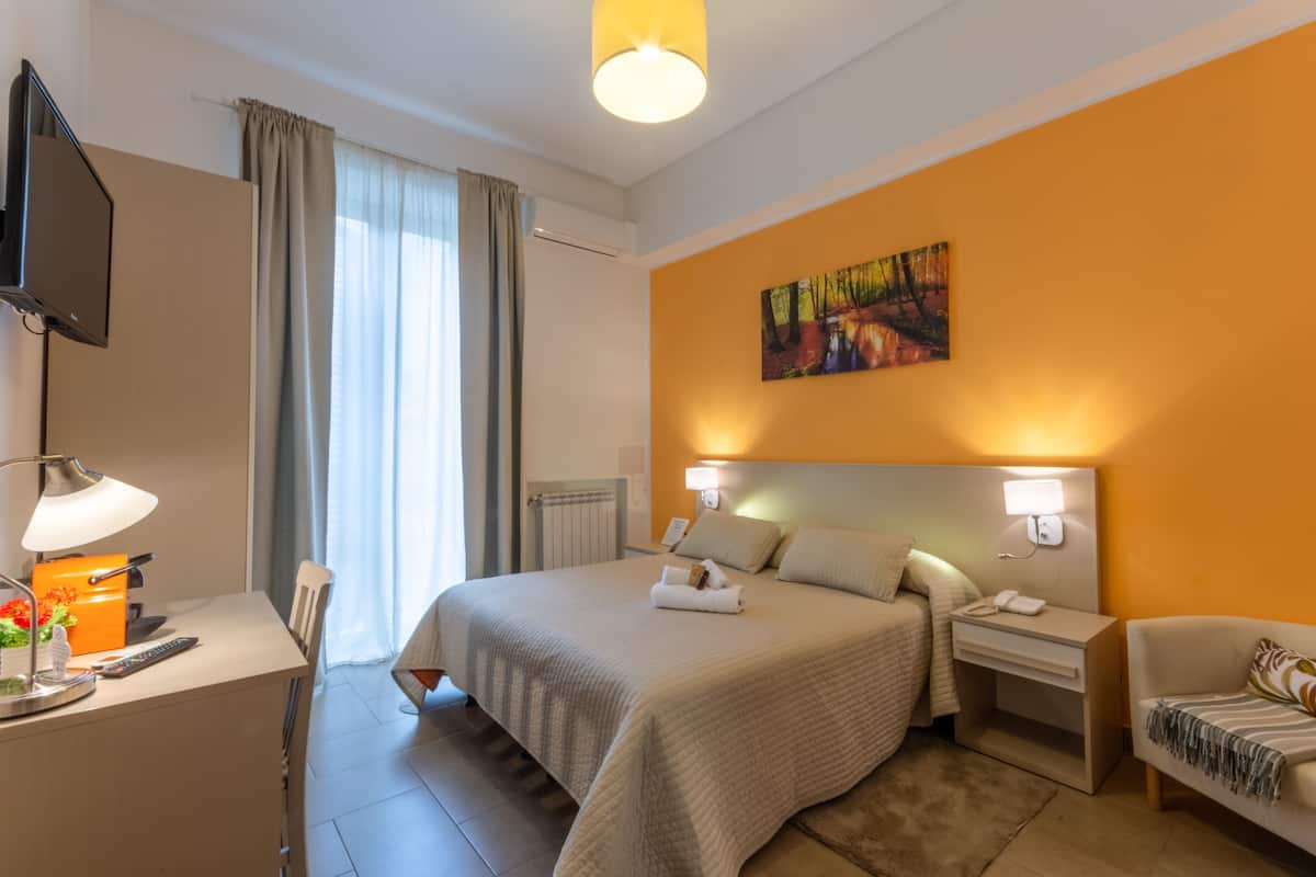 Una habitación de hotel con una cama, mesitas de noche, un escritorio con lámpara, un televisor y un cuadro en la pared.