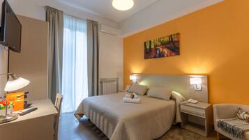 Una habitación de hotel con una cama, mesitas de noche, un escritorio con lámpara, un televisor y un cuadro en la pared.