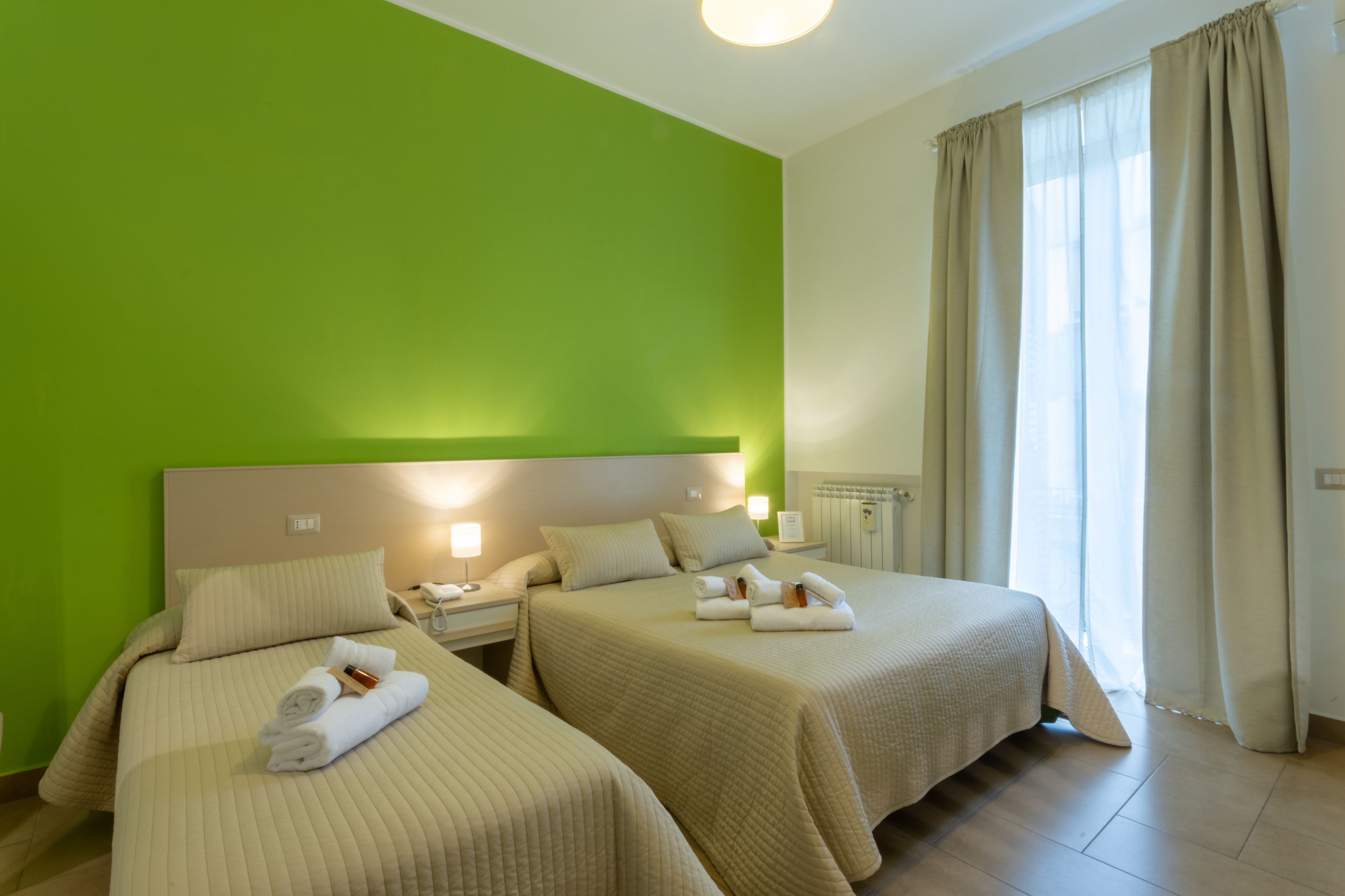 Een hotelkamer met twee bedden, een groene accentmuur en een raam met gordijnen.