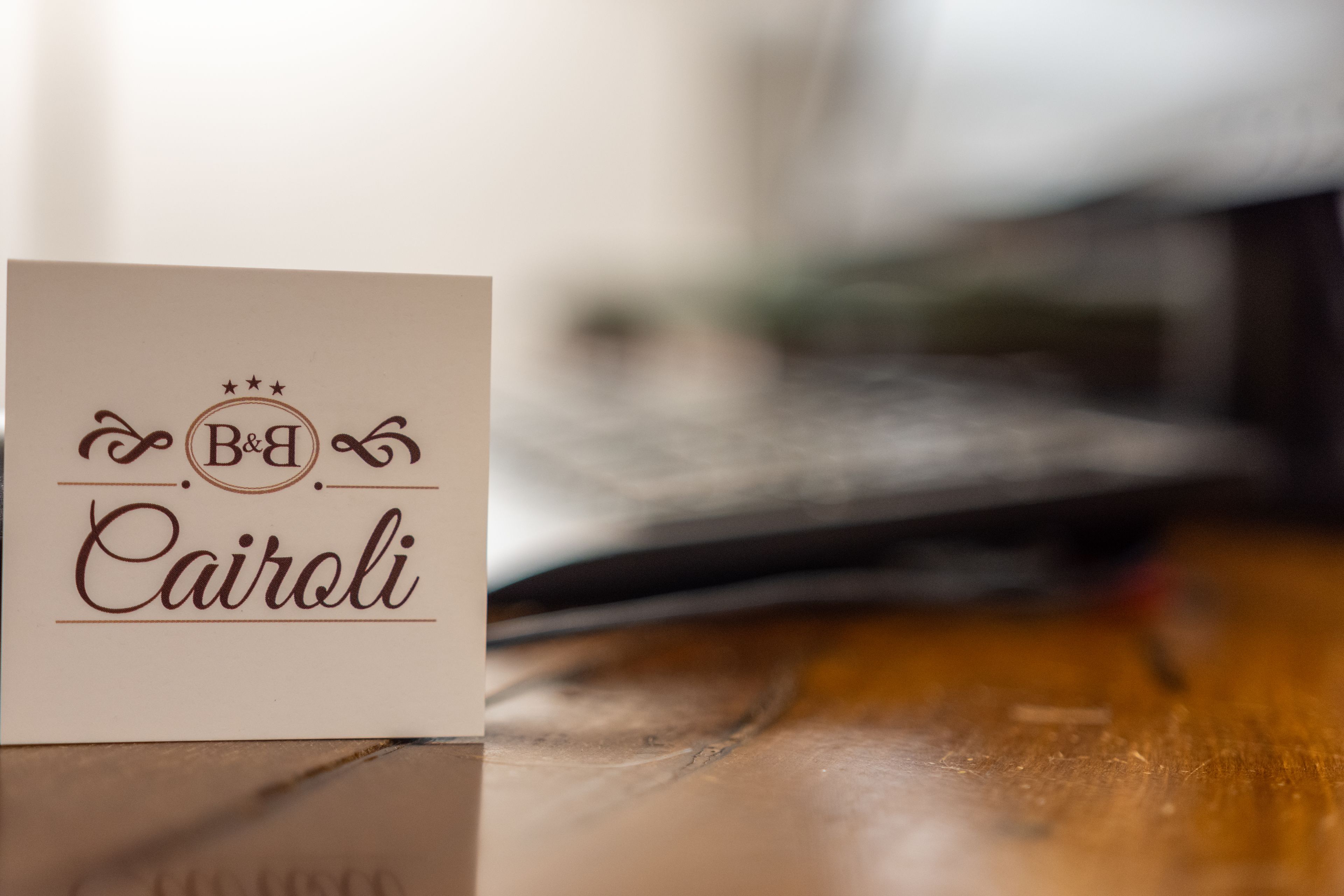 Une carte de visite sur laquelle on peut lire « B&B Cairoli », posée sur une surface en bois.