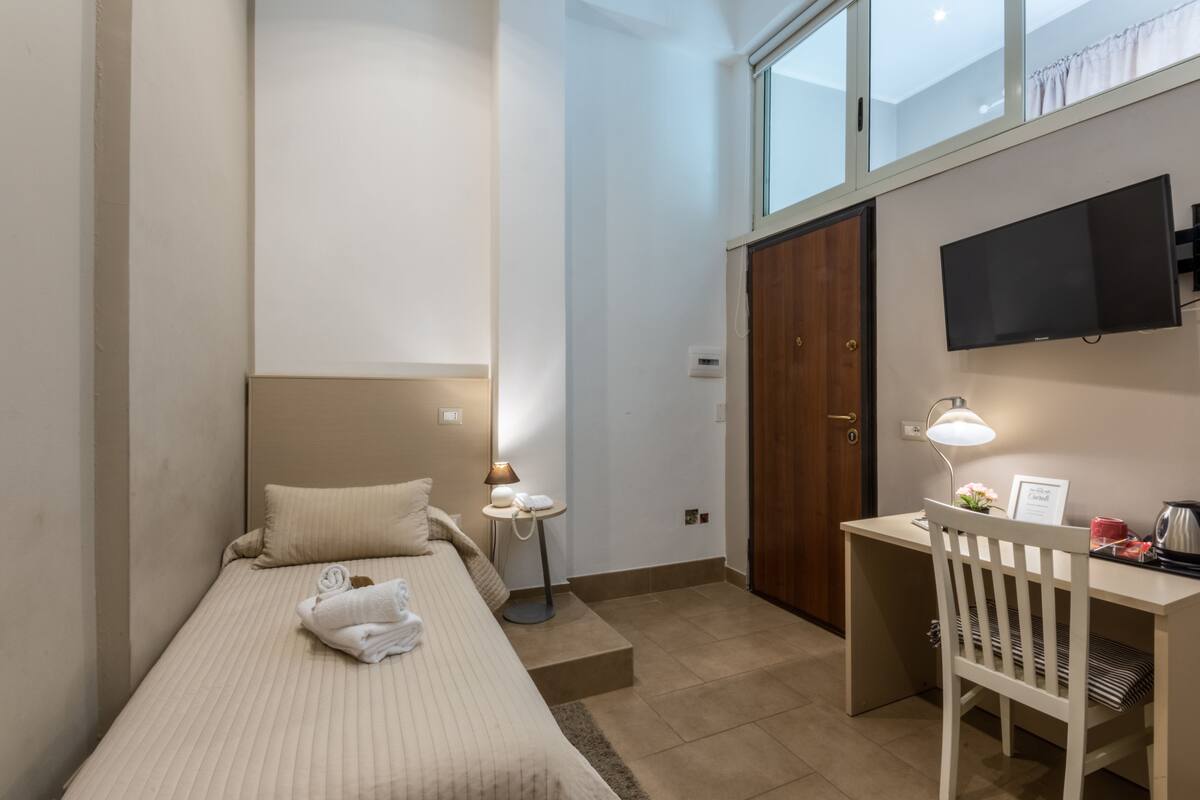 Habitación de hotel con cama, escritorio, silla, televisor y ventana.