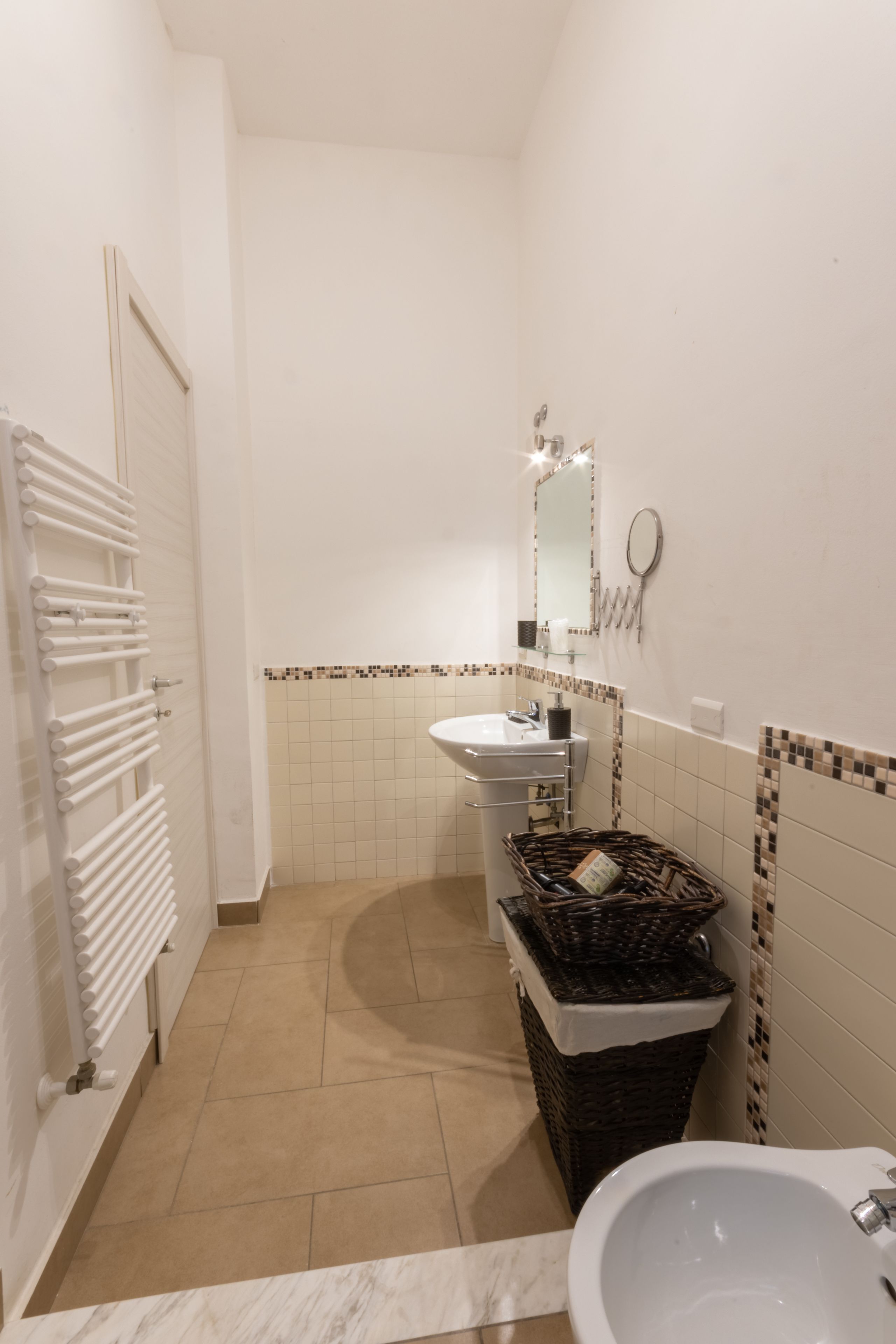 Een badkamer met een witte wastafel, een spiegel, een handdoekhouder en een rieten mandje.