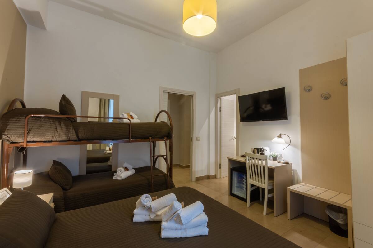 Una habitación de hotel con literas, un escritorio, una silla, un televisor y una lámpara.