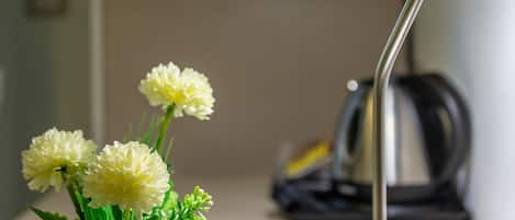 Una lámpara de escritorio con pantalla blanca y base metálica, ubicada junto a un jarrón blanco con follaje verde y flores blancas.