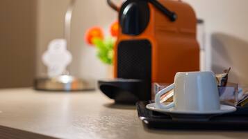 A coffee maker, a white cup, and a small plant on a table.