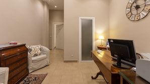 A hotel room with a wooden desk, a computer, a clock, a sofa, and a dresser. - B&B Cairoli (Messina)
