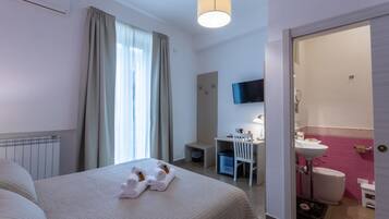 Una habitación de hotel con cama, escritorio, silla, televisión y baño.