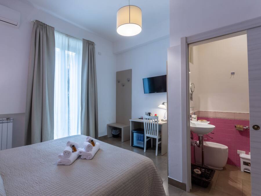 Una habitación de hotel con cama, escritorio, silla, televisión y baño.
