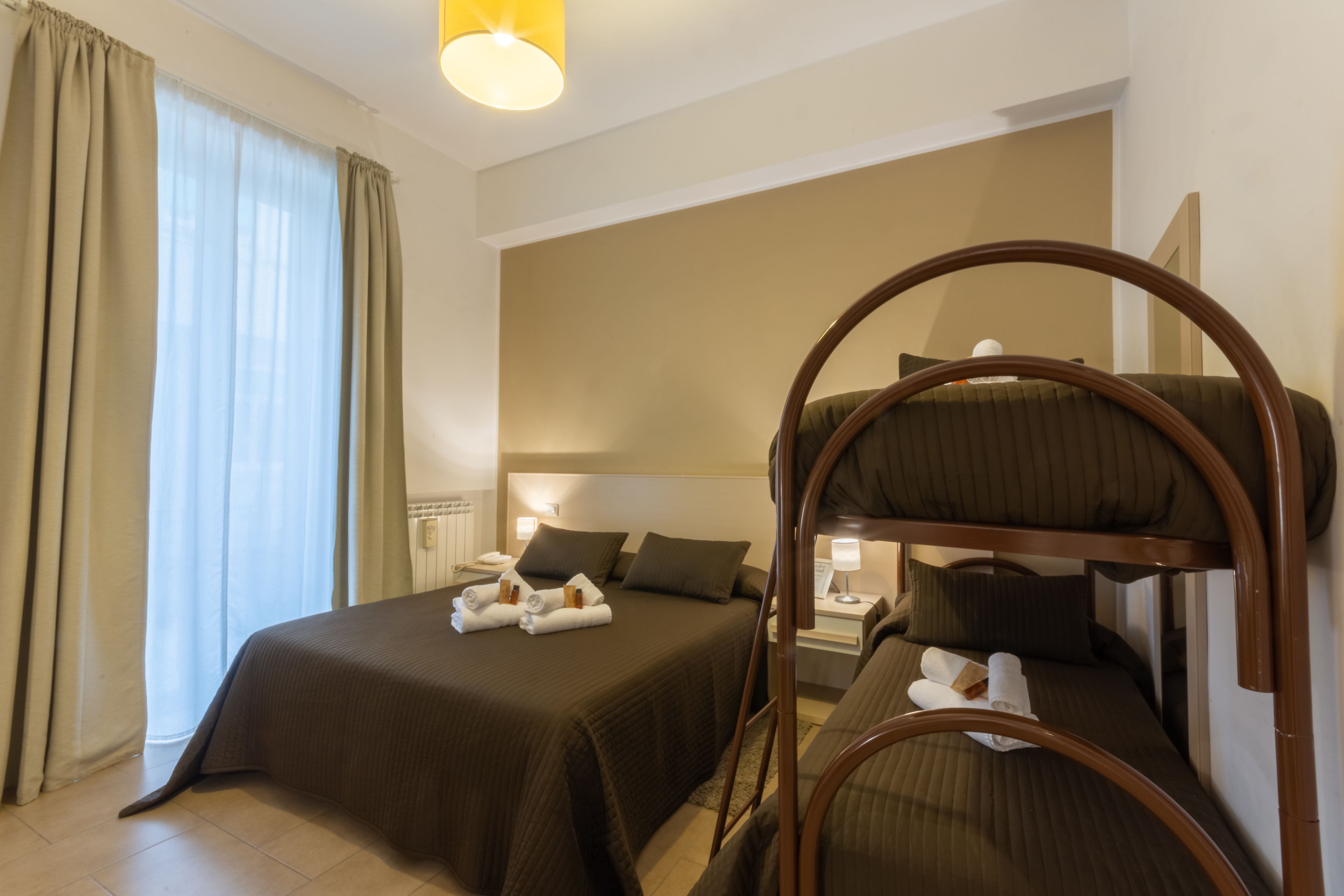 A hotel room with a bunk bed, a single bed, and a bedside table with a lamp.
