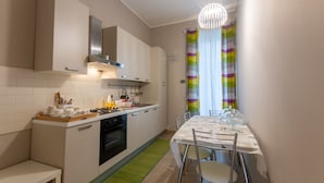 A modern kitchen with white cabinets, a dining table with chairs, and a colorful striped curtain. - B&B Cairoli (Messina)