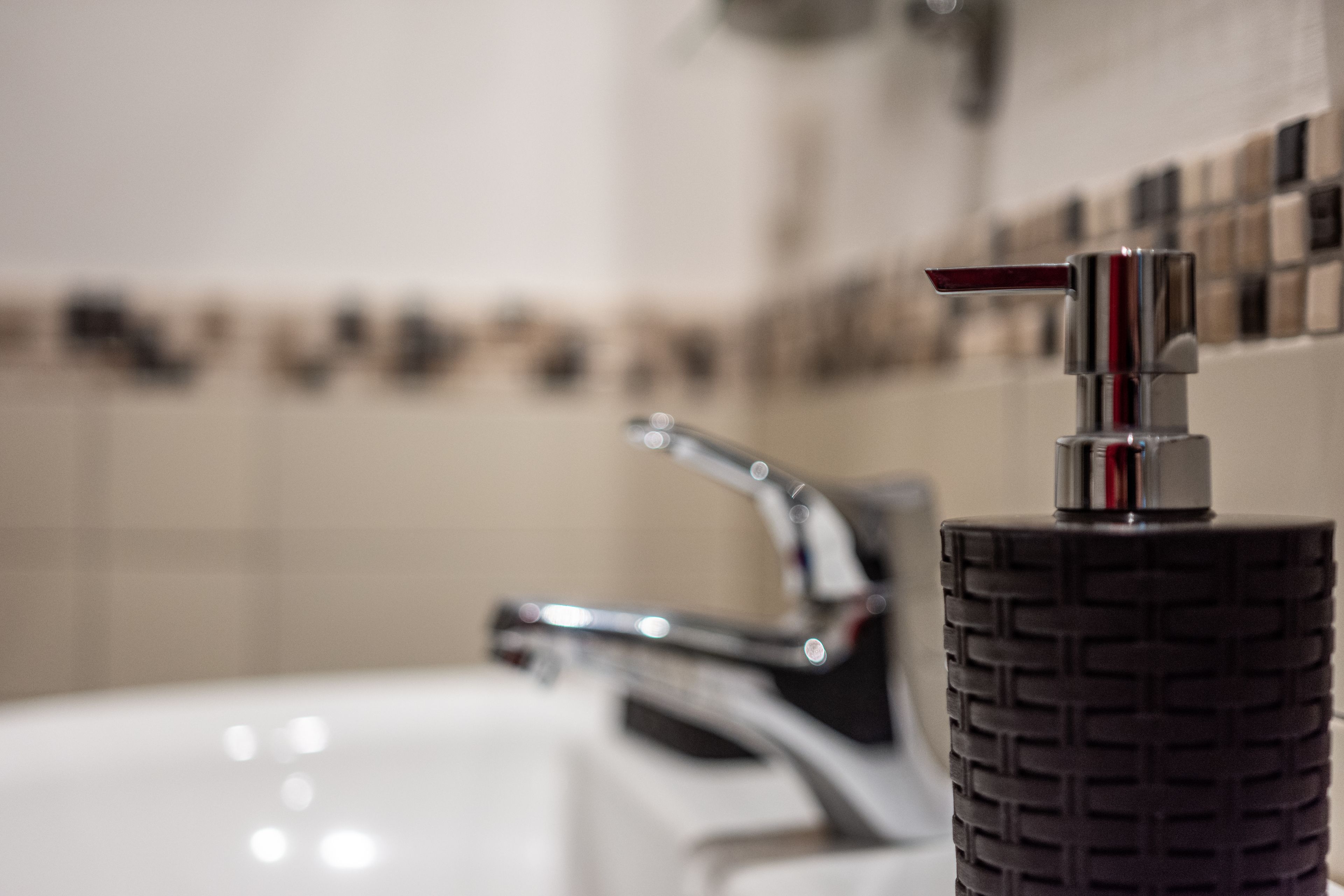 A bathroom with a white sink, a chrome faucet, and a textured soap dispenser.