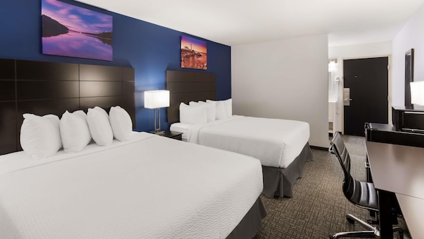 A hotel room with two beds, a desk, a chair, and two wall-mounted paintings. - SureStay by Best Western Presque Isle (Presque Isle)