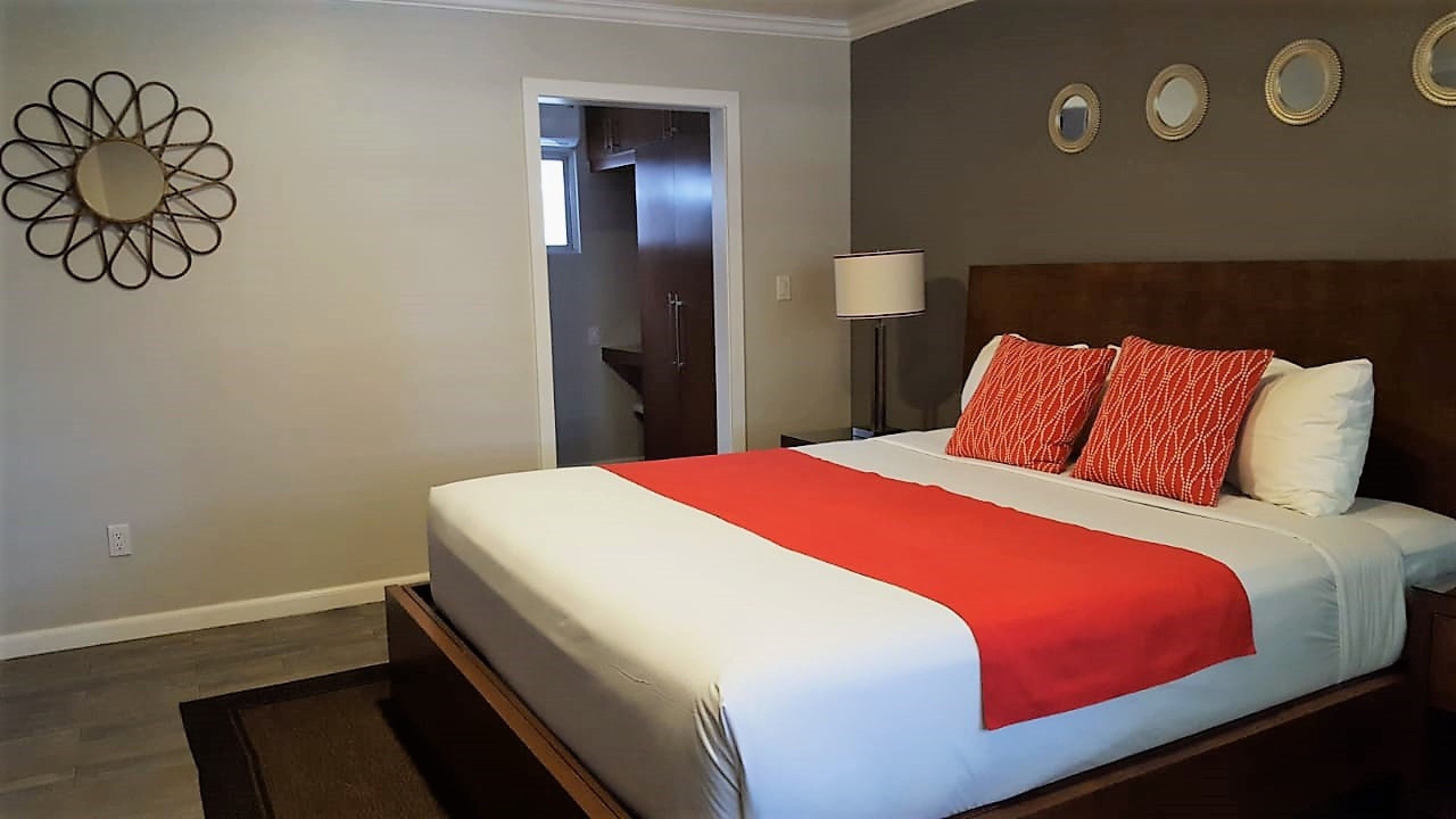 A hotel room with a bed, a nightstand, a lamp, and a door leading to a bathroom.