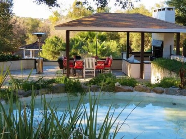 A covered outdoor area with a pool, seating, and a grill.