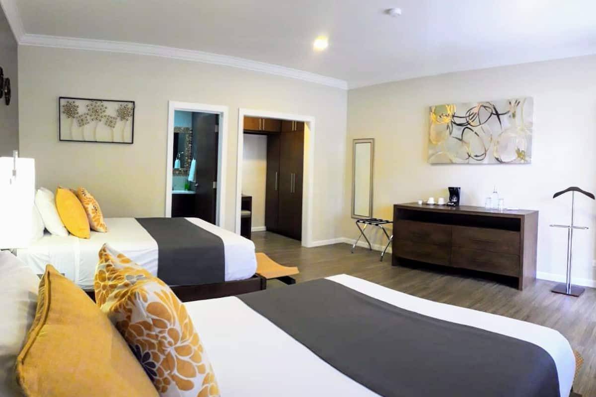 A hotel room with two beds, a dresser, a mirror, and artwork on the walls.