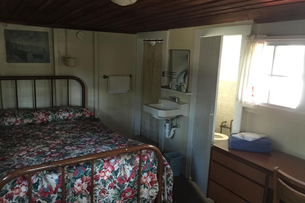A bedroom with a bed, a wooden dresser, a sink, and a window.
