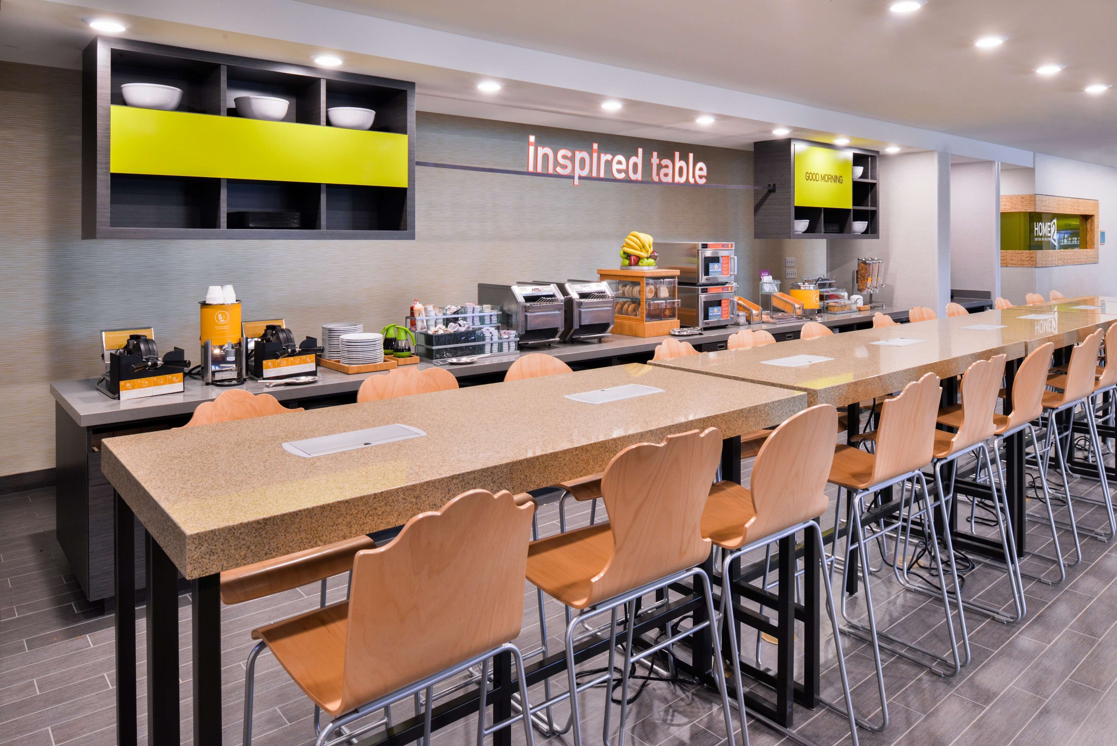 Une longue table à manger collective, avec des chaises, un coin café et un panneau indiquant « table d’inspiration ».