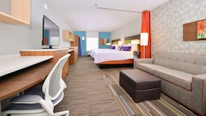 Una habitación de hotel moderna con escritorio, silla, cama, sofá y televisor.