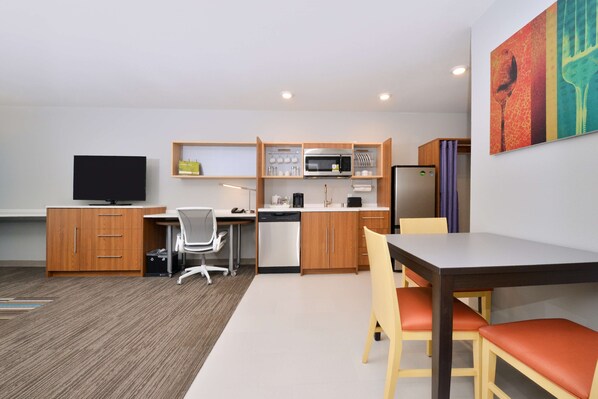 A compact hotel room with a kitchenette, a dining area, and a TV.