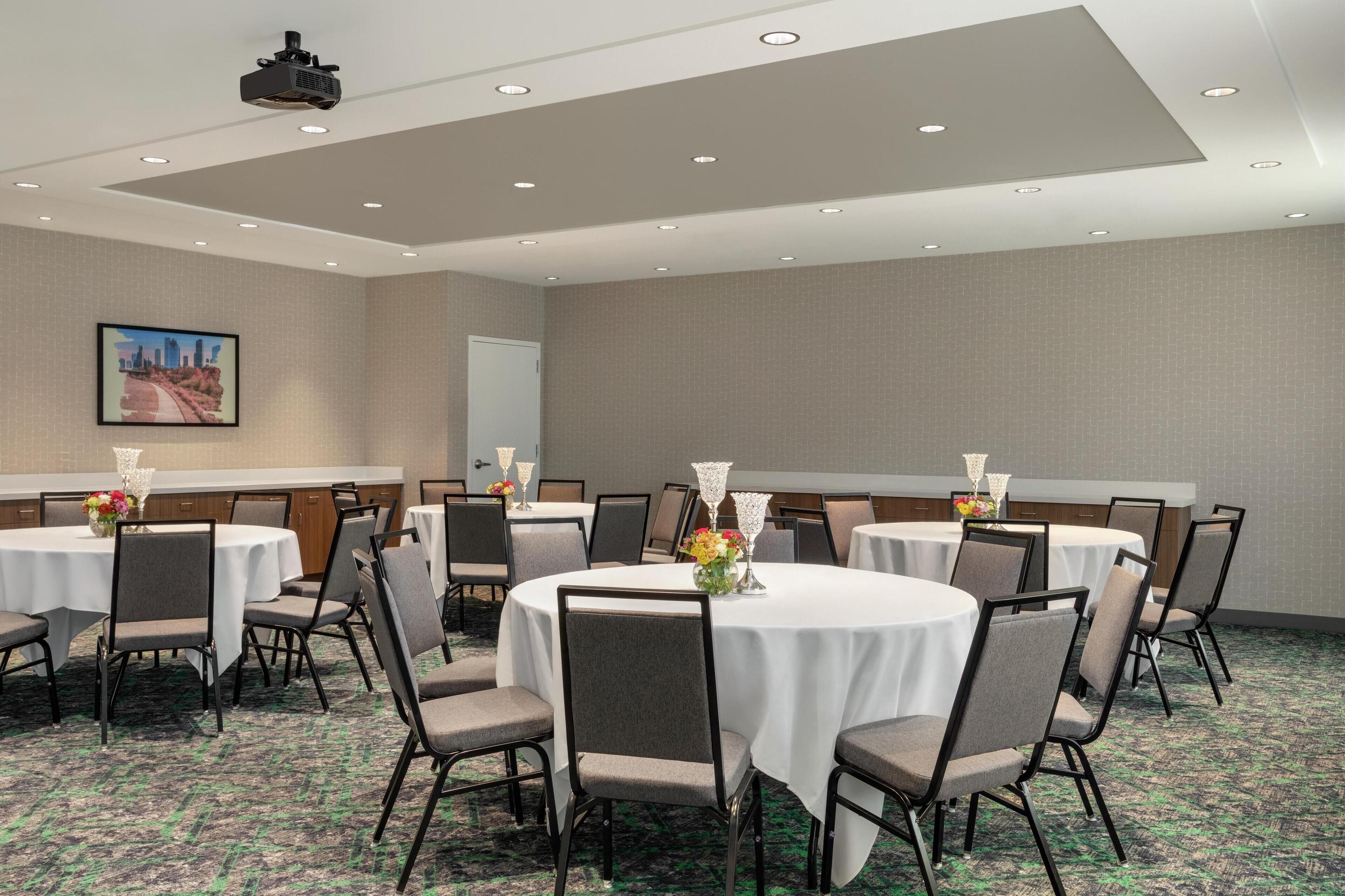 A conference room with multiple round tables, chairs, and a projector on the ceiling.