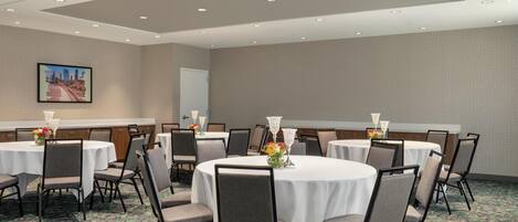 A conference room with multiple round tables, chairs, and a projector on the ceiling.