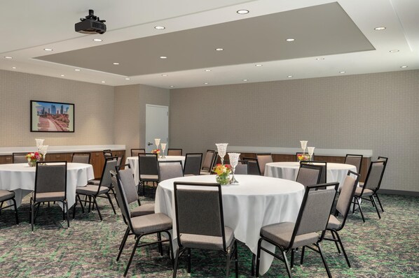 A conference room with multiple round tables, chairs, and a projector on the ceiling.