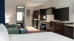 A hotel room with a bed, a desk, a chair, a TV, a mirror, and a small seating area. - Home2 Suites by Hilton Houston Energy Corridor (Houston)