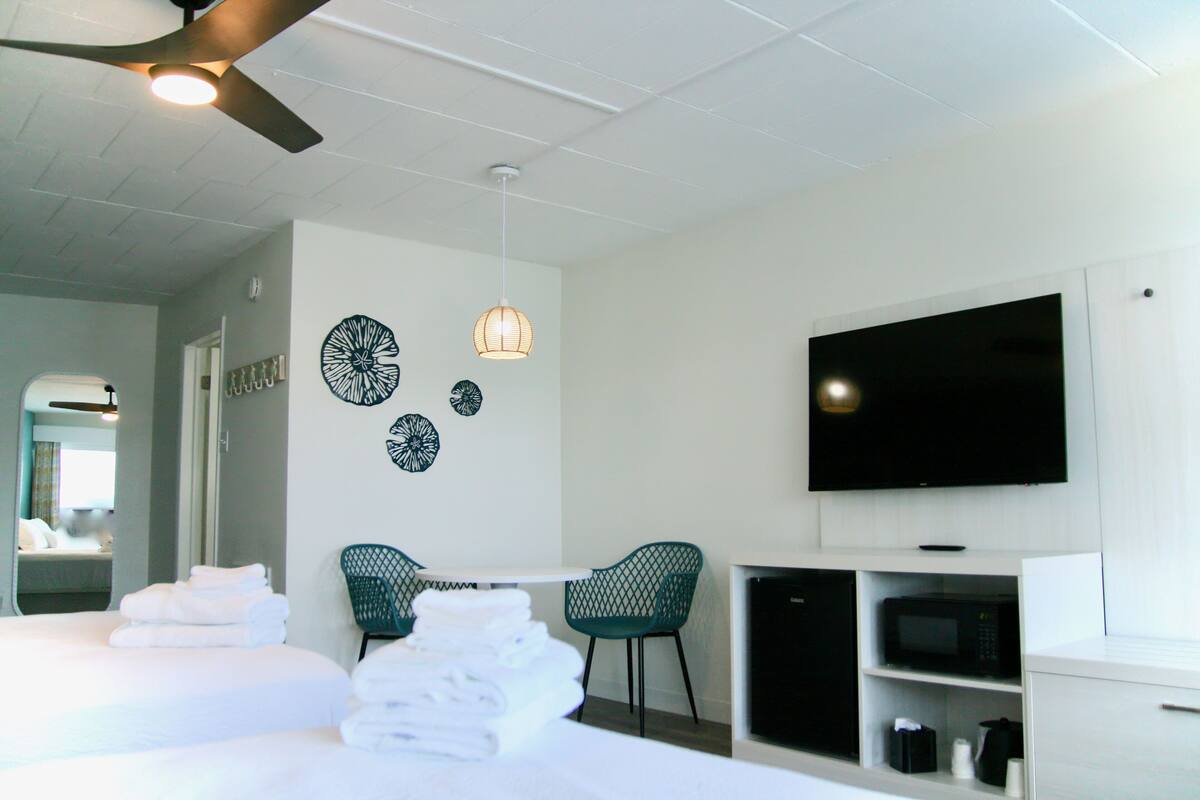 A hotel room with a bed, two chairs, a flat-screen TV, a microwave, and a ceiling fan.