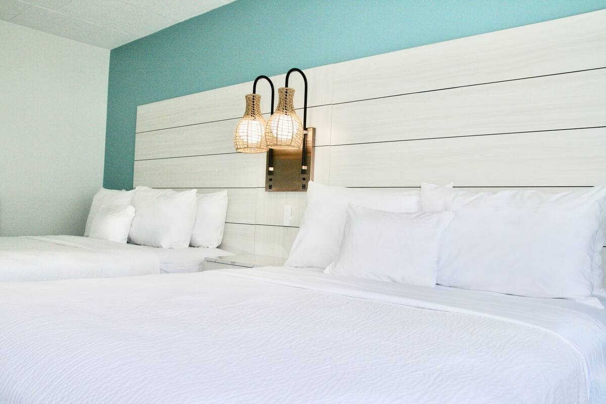 A hotel room with two beds, a light blue accent wall, and a wall-mounted light fixture.