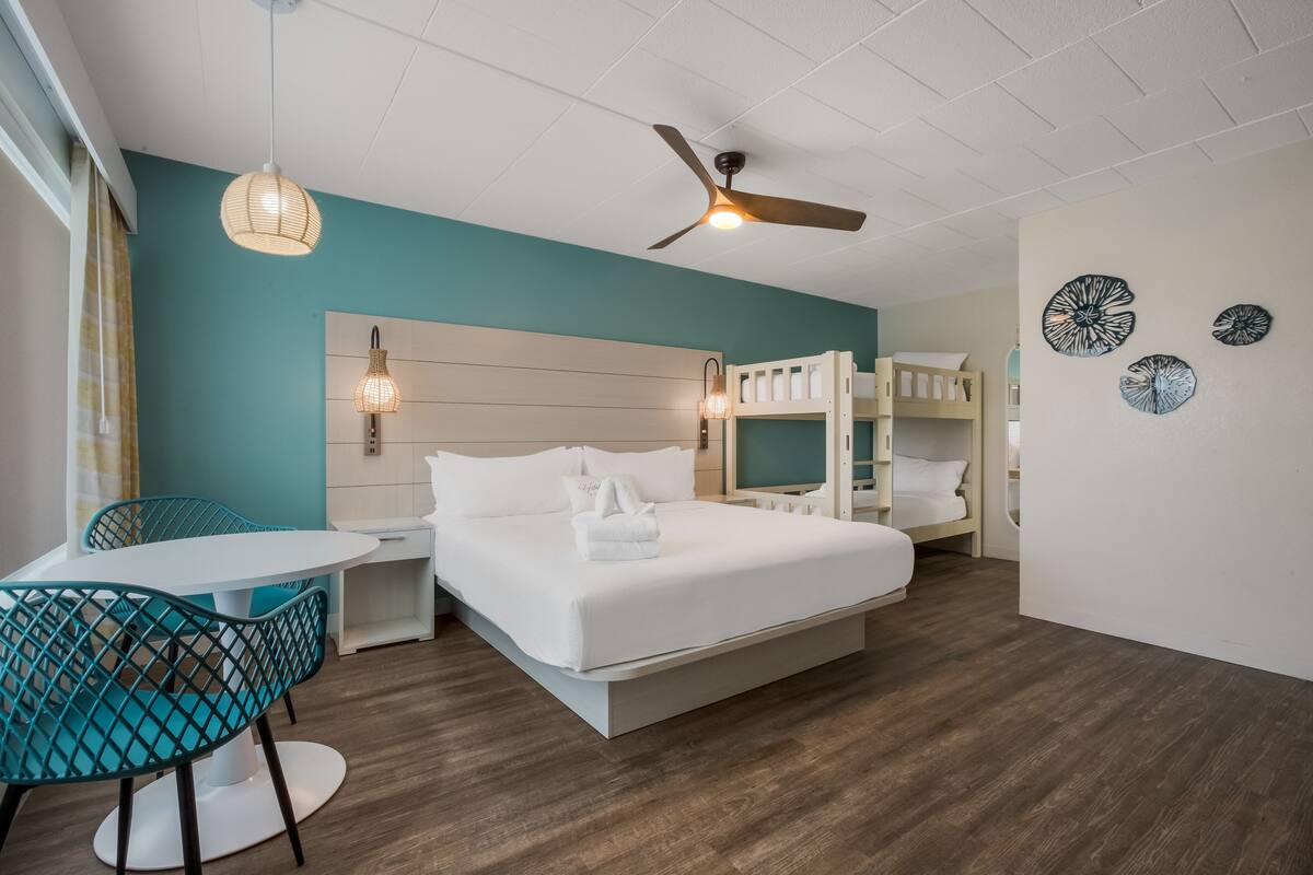 A hotel room with a bed, a desk, a chair, a ceiling fan, and bunk beds.
