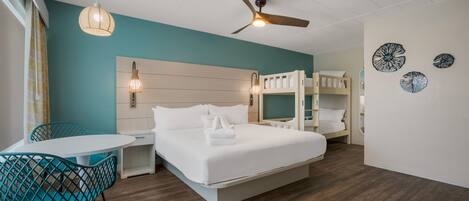 Habitación de hotel con cama, escritorio, silla, ventilador de techo y literas.