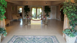Un hall d’entrée avec une barrière en forme de corde rouge, un comptoir d’accueil et une vue sur l’extérieur.