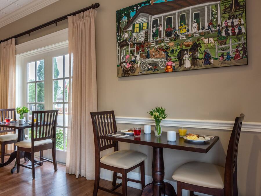 A dining area with a table set for four, a painting above the table, and a window with curtains.
