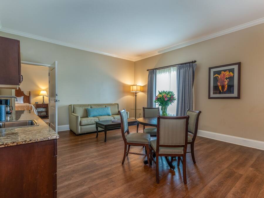 A modern living room with a dining area, wooden flooring, a kitchen with a granite countertop, and a large window with curtains.