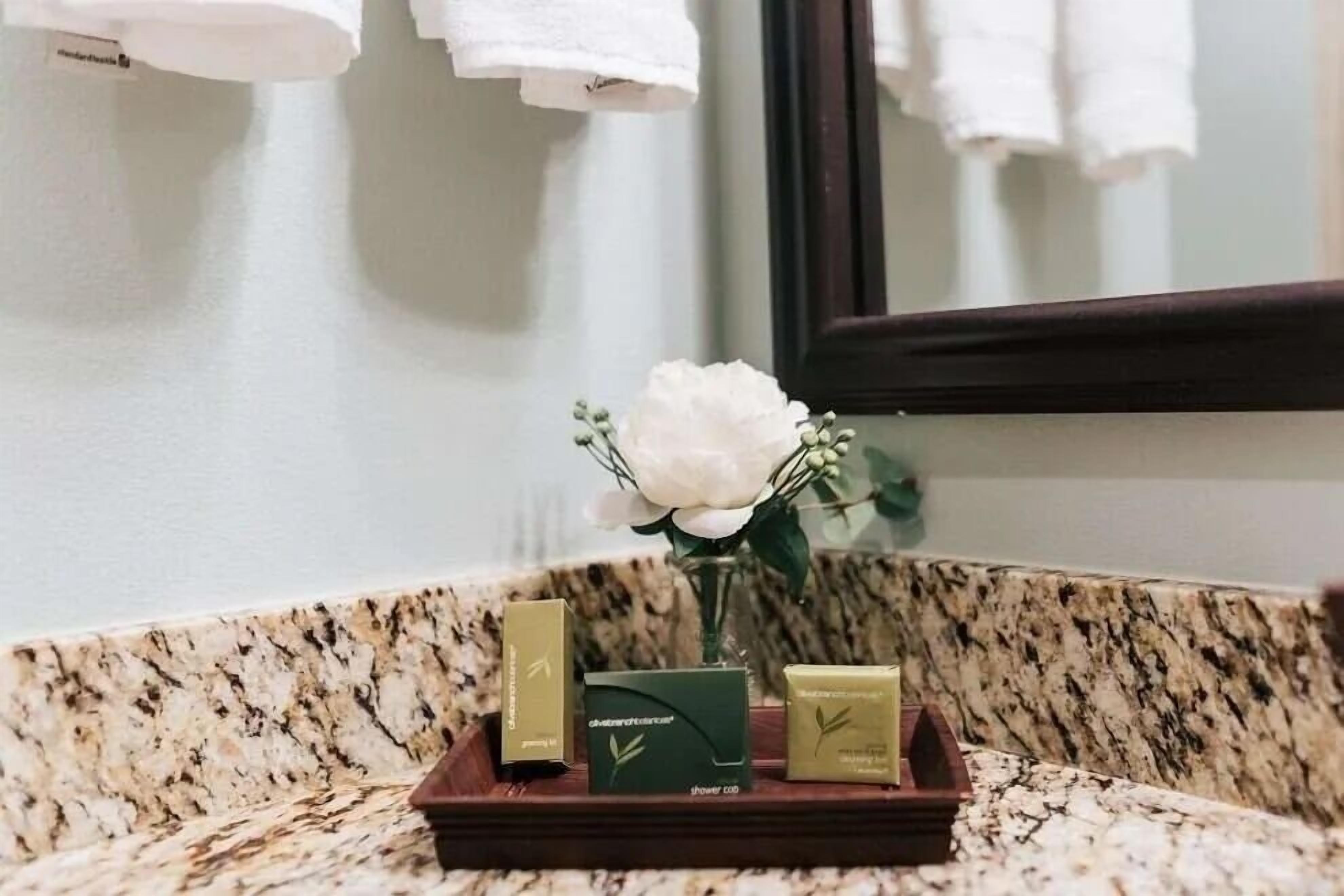 A bathroom vanity with a marble countertop, a white flower vase, and three toiletries in a wooden tray.