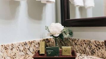 A bathroom vanity with a marble countertop, a white flower vase, and three toiletries in a wooden tray.