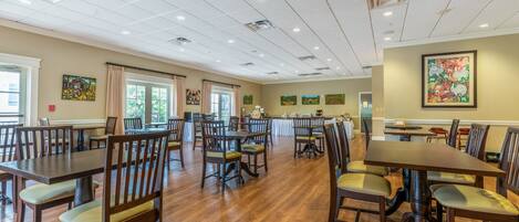 A spacious dining area with multiple tables and chairs, a kitchen in the background, and artwork on the walls.