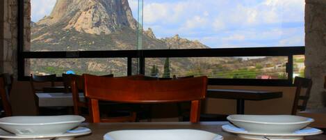 Une table à manger dressée avec des assiettes, des couverts, et une vue sur une montagne par la fenêtre.