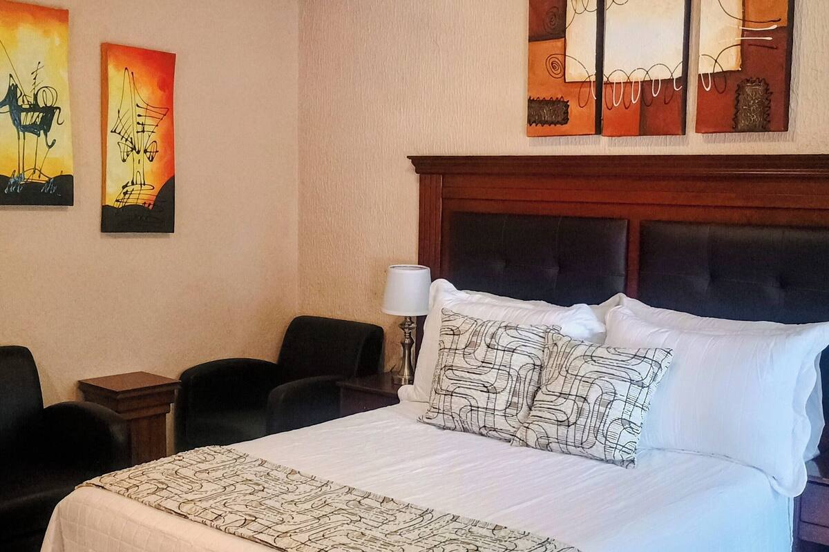 A hotel room with a large bed, two chairs, a nightstand, and a ceiling light.