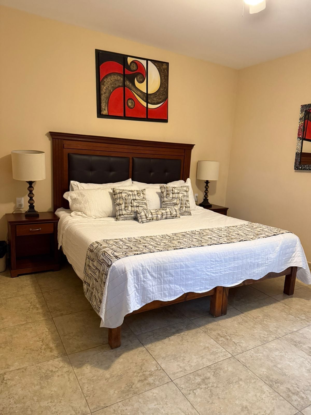 A hotel room with a large bed, two bedside tables, a headboard, and a wall art piece.