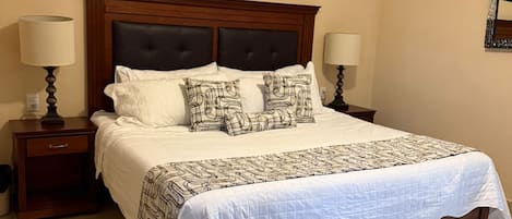A hotel room with a large bed, two bedside tables, a headboard, and a wall art piece.