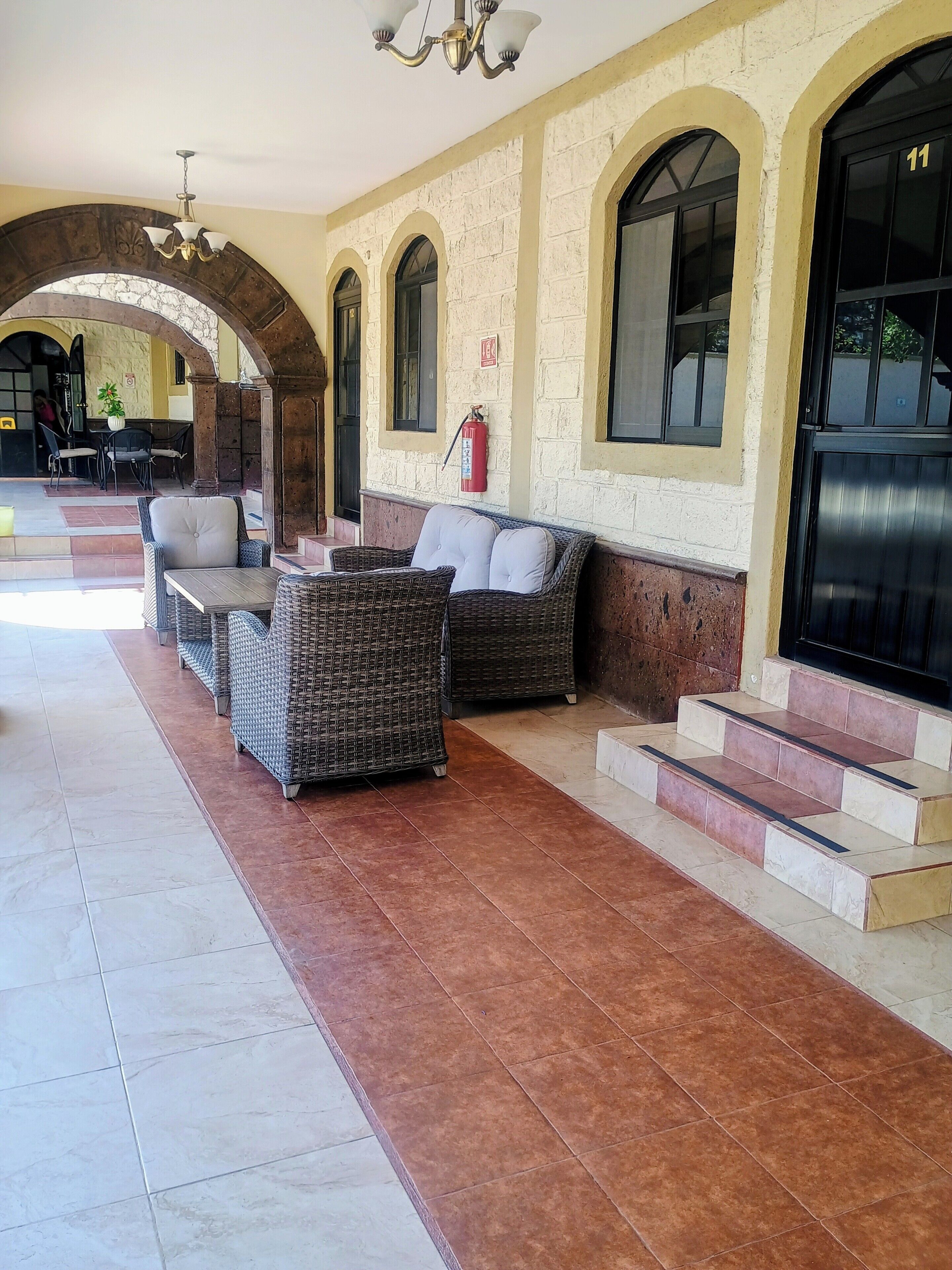 A covered outdoor seating area with wicker furniture and a fire extinguisher on the wall.